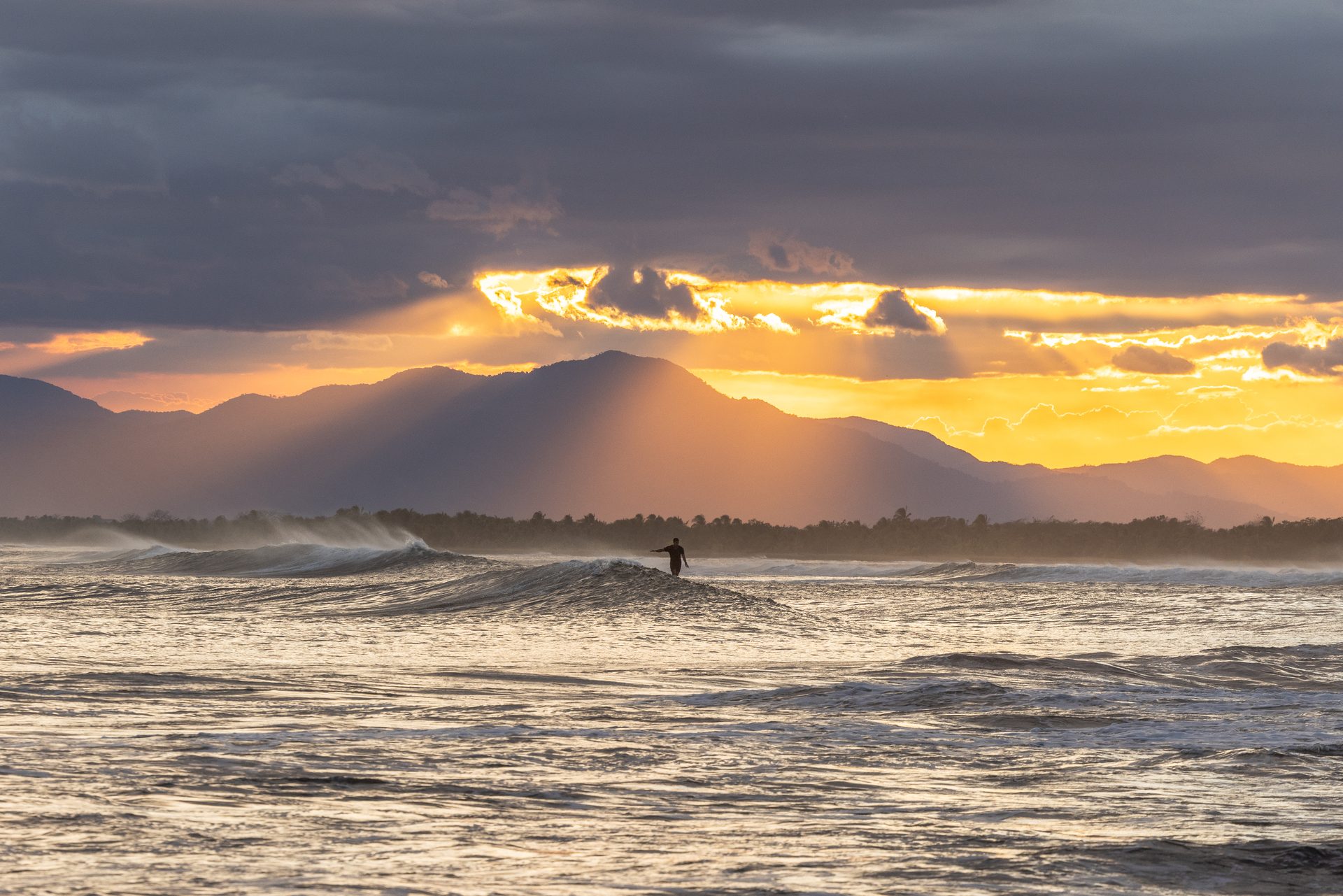 A lone surfer on a wave under a golden sunset sky